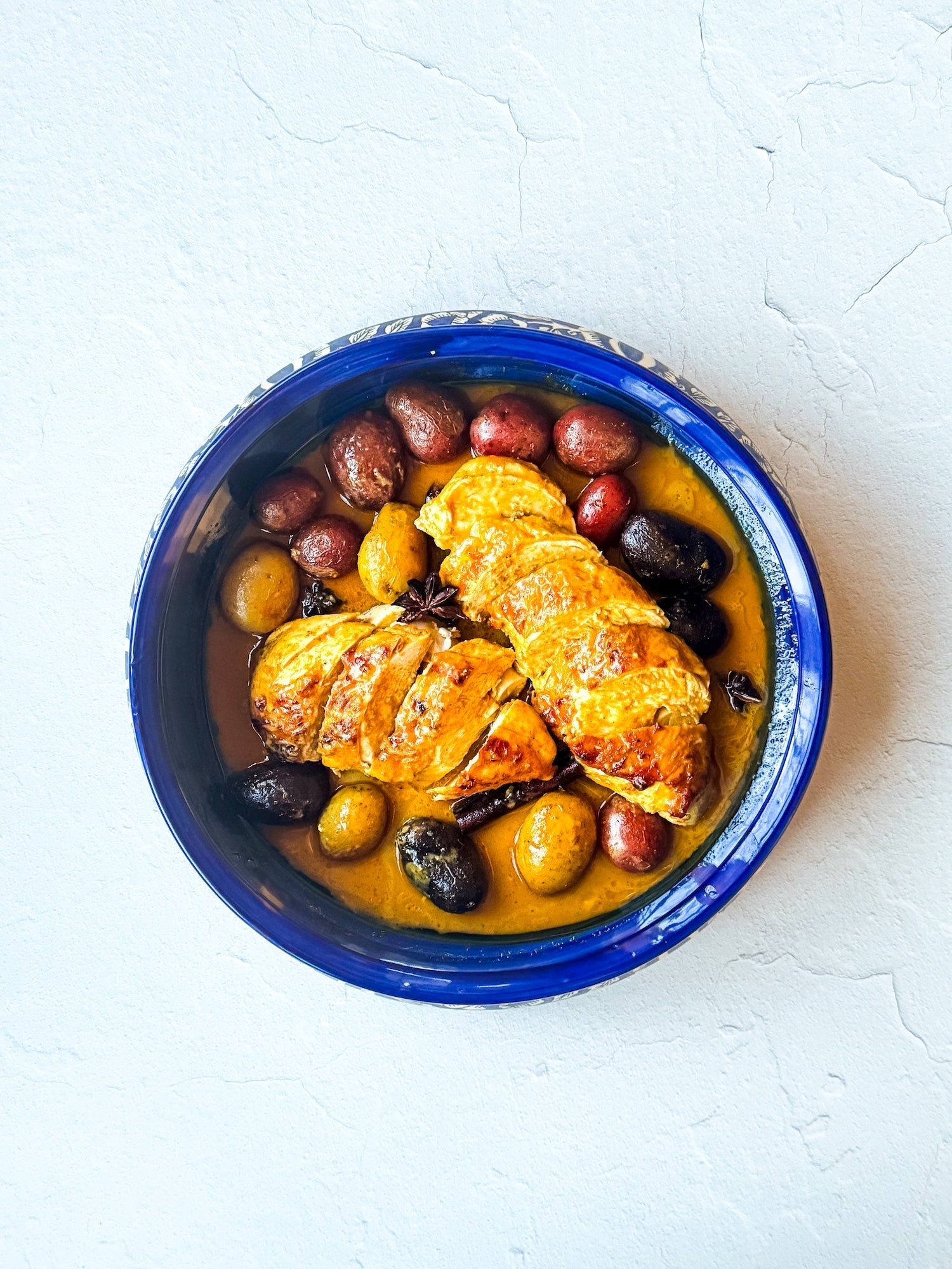 Baked chicken and potatoes topped with creamy Thai coconut curry sauce, served in a rustic baking dish and garnished with fresh herbs.