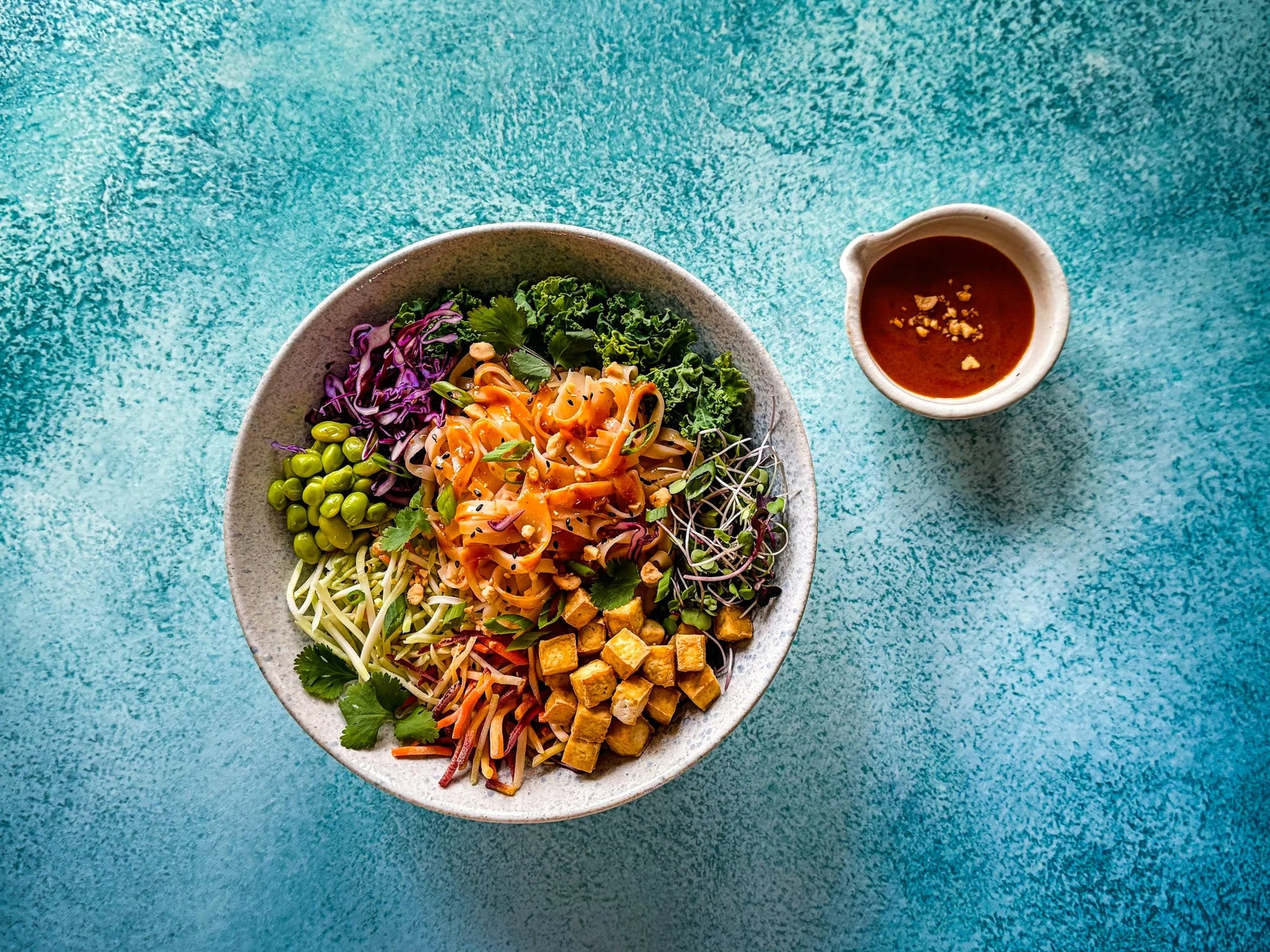 Large bowl of Asian noodle salad with colourful vegetables and peanut sauce drizzle, topped with sesame seeds
